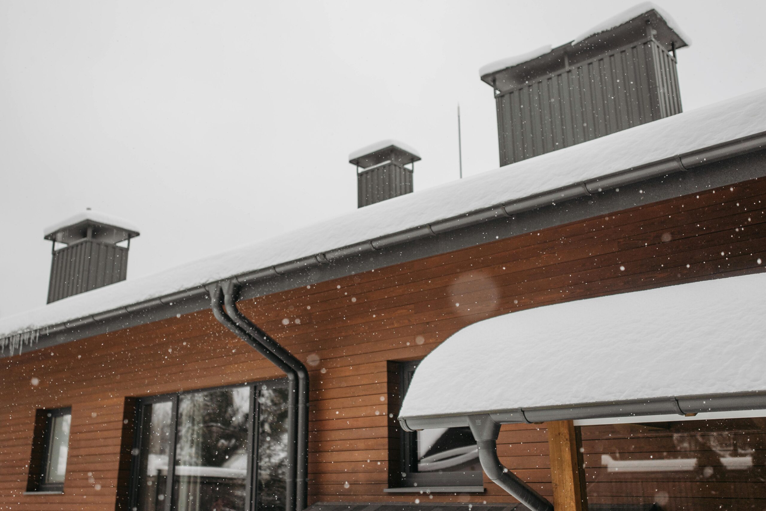 A close-up of a snow-covered roof with chimneys during winter snowfall, highlighting winter storm damage